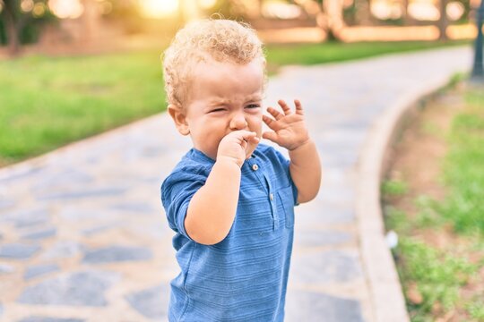 Cute and sad little boy crying having a tantrum at the park on a sunny day. Beautiful blonde hair male toddler frustrated with tears on face outdoors