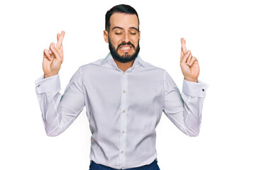 Young man with beard wearing business shirt gesturing finger crossed smiling with hope and eyes closed. luck and superstitious concept.