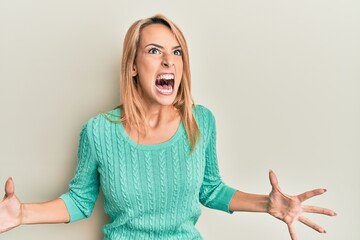 Beautiful blonde woman wearing casual winter sweater crazy and mad shouting and yelling with...