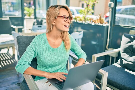 Young blonde woman smiling happy working using laptop sitting at the coffee shop terrace.