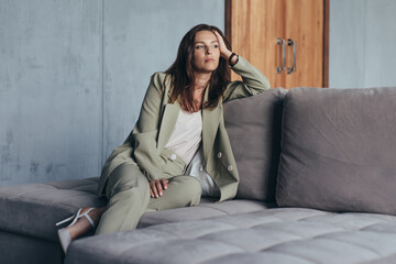 Woman in the suit sits on the couch thoughtfully