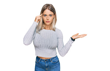 Beautiful blonde woman wearing casual clothes confused and annoyed with open palm showing copy space and pointing finger to forehead. think about it.