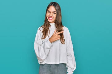 Young brunette woman wearing casual turtleneck sweater cheerful with a smile of face pointing with hand and finger up to the side with happy and natural expression on face