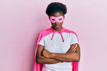 Young african american girl wearing superhero mask and cape costume skeptic and nervous,...