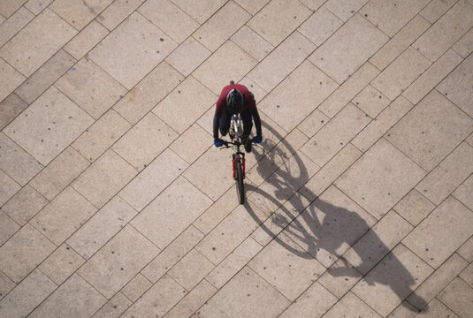 Ciclista a andar na bicicleta numa cal&ccedil;ada de pedra em ambiente citadino, vista de cima, fotografia a&eacute;rea