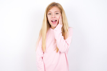 Shocked, astonished beautiful caucasian little girl wearing pink hoodie looking surprised in full disbelief wide open mouth with hand near face. Positive emotion facial expression body language.