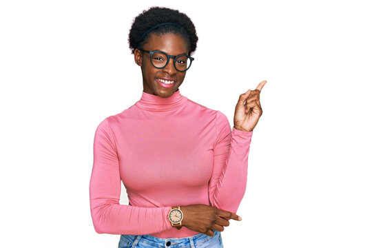 Young african american girl wearing casual clothes and glasses with a big smile on face, pointing with hand and finger to the side looking at the camera.