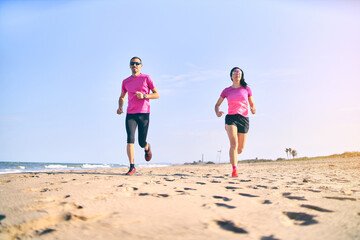 Young fit couple running towards the camera on the beach during sunrise. Healthy start of the day. Wearing pink and black sportswear. Running by the sea. Healthy lifestyle.