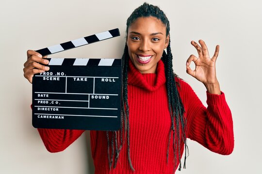 African American Woman With Braids Holding Video Film Clapboard Doing Ok Sign With Fingers, Smiling Friendly Gesturing Excellent Symbol