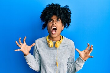 African american woman with afro hair wearing sweatshirt and using headphones crazy and mad shouting and yelling with aggressive expression and arms raised. frustration concept.