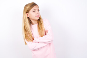 Image of upset beautiful caucasian little girl wearing pink hoodie over white background with arms crossed. Looking with disappointed expression aside after listening to bad news.