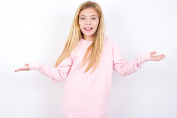 So what? Portrait of arrogant beautiful caucasian little girl wearing pink hoodie over white background shrugging hands sideways smiling gasping indifferent, telling something obvious.