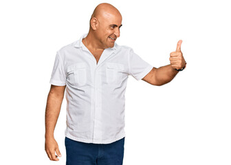 Mature middle east man with mustache wearing casual white shirt looking proud, smiling doing thumbs up gesture to the side