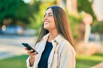 Young hispanic girl smiling happy using smartphone at the park.