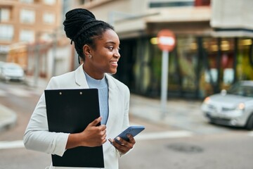 Young african american businesswoman using smartphone holding clipboard at the city.