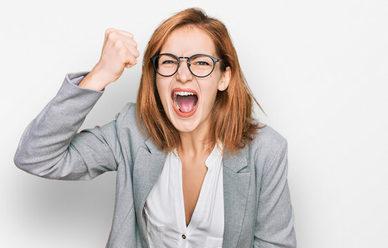 Young caucasian woman wearing business style and glasses angry and mad raising fist frustrated and furious while shouting with anger. rage and aggressive concept.