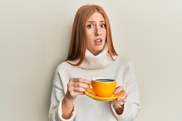 Young irish woman drinking a cup of coffee clueless and confused expression. doubt concept.
