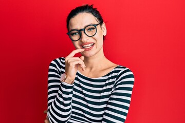 Young caucasian woman wearing casual clothes and glasses looking confident at the camera with smile with crossed arms and hand raised on chin. thinking positive.