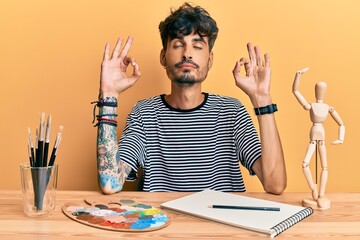 Young hispanic man sitting on the table at art studio relax and smiling with eyes closed doing...