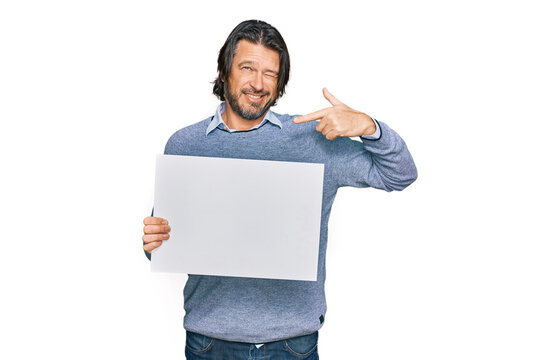 Middle age handsome man holding blank empty banner pointing finger to one self smiling happy and proud