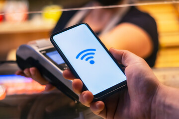 Customer is paying with smartphone in shop using NFC technology. against the background of the payment terminal and the seller's girl.