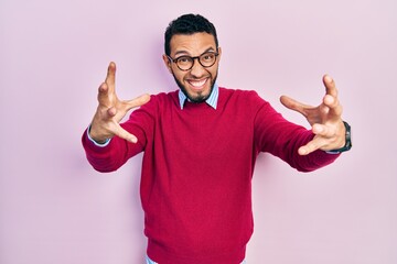 Hispanic man with beard wearing business shirt and glasses shouting frustrated with rage, hands trying to strangle, yelling mad