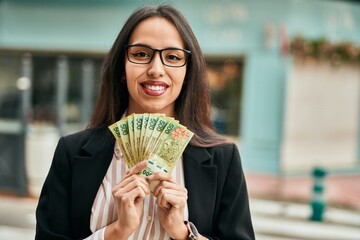 Young hispanic businesswoman holding argentina pesos banknotes at the city. - obrazy, fototapety, plakaty
