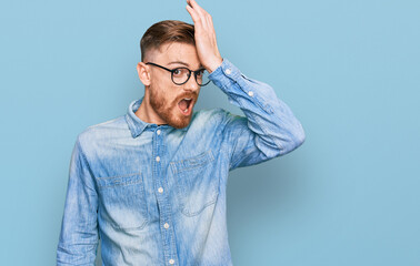 Young redhead man wearing casual denim shirt surprised with hand on head for mistake, remember...