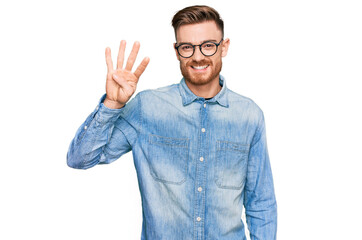 Young redhead man wearing casual denim shirt showing and pointing up with fingers number four while smiling confident and happy.