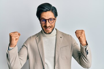 Young hispanic man wearing business jacket and glasses celebrating surprised and amazed for success...