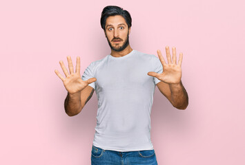 Young hispanic man wearing casual white t shirt afraid and terrified with fear expression stop...