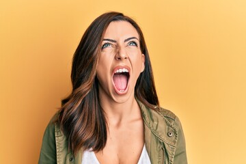 Young brunette woman wearing casual clothes over yellow background angry and mad screaming frustrated and furious, shouting with anger looking up.