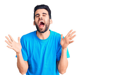Fototapeta premium Young handsome man with beard wearing casual t-shirt celebrating mad and crazy for success with arms raised and closed eyes screaming excited. winner concept