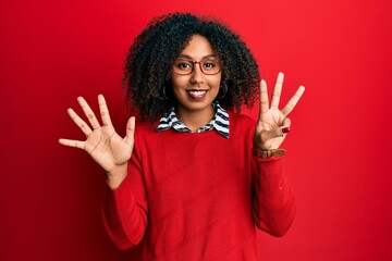 Beautiful african american woman with afro hair wearing sweater and glasses showing and pointing up with fingers number eight while smiling confident and happy.