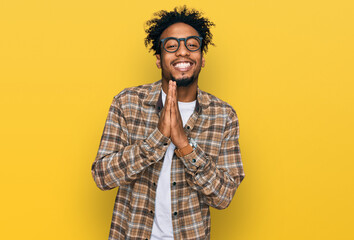 Young african american man with beard wearing casual clothes and glasses praying with hands together asking for forgiveness smiling confident.