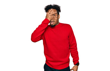 Young african american man with beard wearing casual winter sweater peeking in shock covering face and eyes with hand, looking through fingers with embarrassed expression.