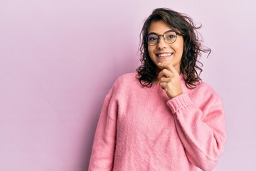 Young hispanic woman wearing casual clothes and glasses smiling looking confident at the camera with crossed arms and hand on chin. thinking positive.