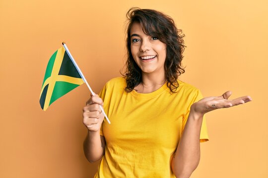 Young hispanic woman holding jamaica flag celebrating achievement with happy smile and winner expression with raised hand