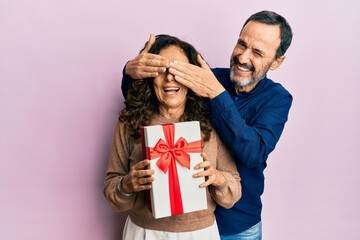 Middle age hispanic couple surprising with gift winking looking at the camera with sexy expression,...