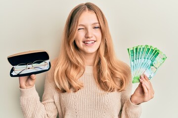 Beautiful young caucasian girl holding glasses and russian ruble banknotes winking looking at the...