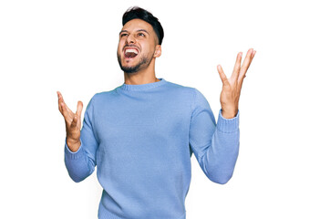Fototapeta premium Young arab man wearing casual clothes crazy and mad shouting and yelling with aggressive expression and arms raised. frustration concept.
