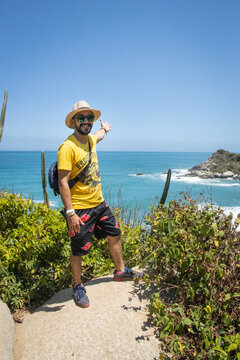 Hombre de vacaciones con camisa amarilla parado en una roca junto al mar azul en un d&iacute;a soleado de verano