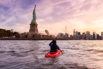 Adventurous Woman Sea Kayaking near the Statue of Liberty. Colorful Sunrise sky Art Render. Taken...