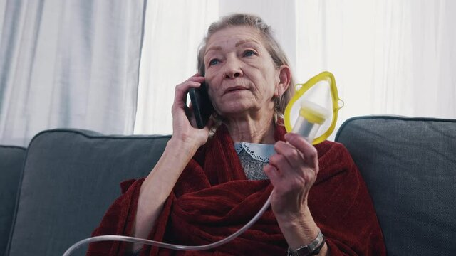Vulnerable old woman having a phone call and using inhaler. Difficulty breathing at old age. High quality 4k footage