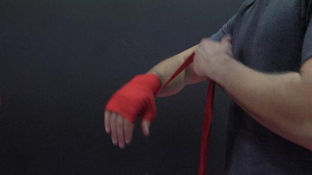 Man ties red bandages for boxing over her hand and prepares for training