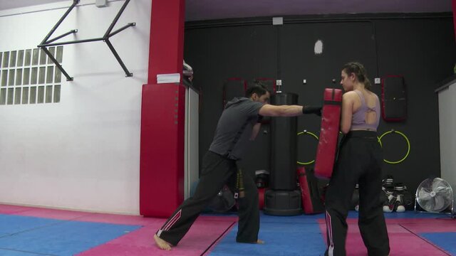 Man trains boxing and kicks on a training device that a woman is holding