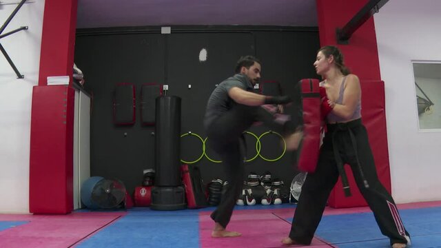 Strong Man trains boxing and kicks on a training device that a woman is holding