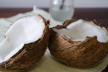 Coconut half and a glass jar with fresh coconut water on wooden table with cloth.