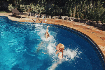 Girls sisters diving in water on home backyard pool. Children siblings friends enjoying and having fun in swimming pool together. Summer outdoor water activity for kids.