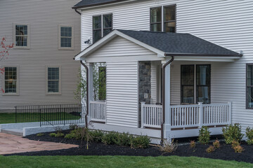 Covered porch with white siding, triange roof, black eaves gutters on a new American house
